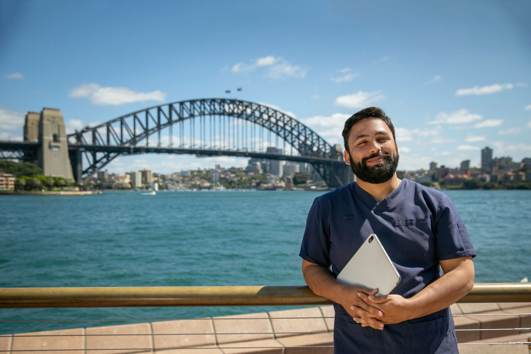 CDU nursing student in front of the Sydney Harbour Bridge holding a laptop