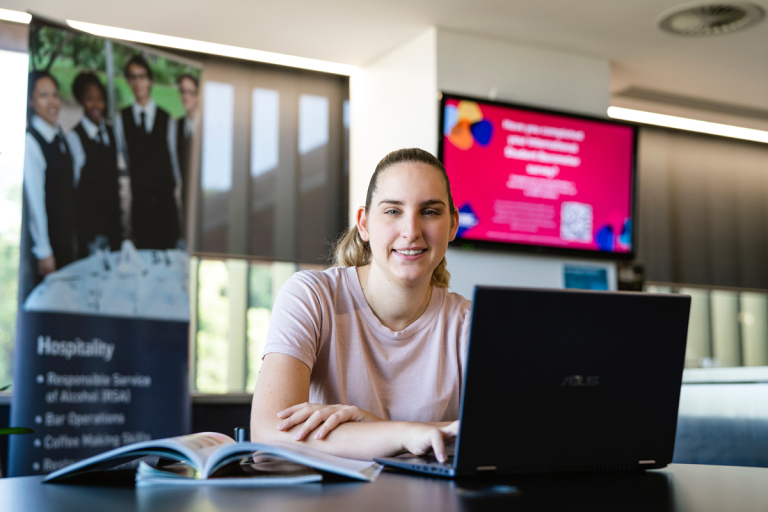 CDU student Zoe White using a laptop in front of hospitality banner