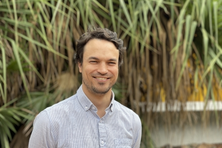 Dr Clement Duvert, head and shoulders, with green spiky-looking leaves hanging down in background