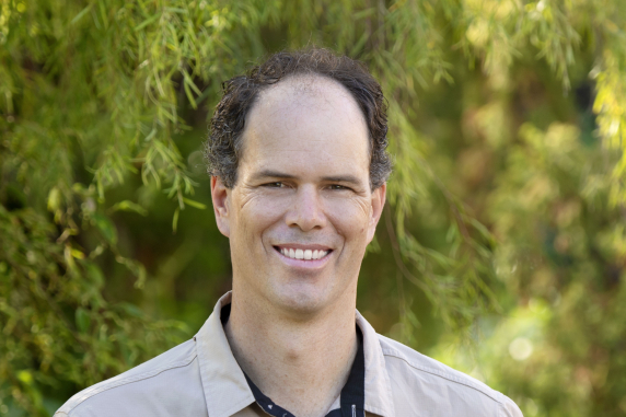 Sam Banks, head and shoulders, with green vegetation behind 
