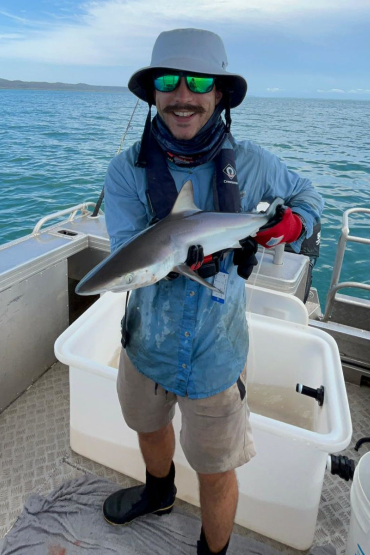 Person wearing hat and sunglasses standing in a boat holding a small shark